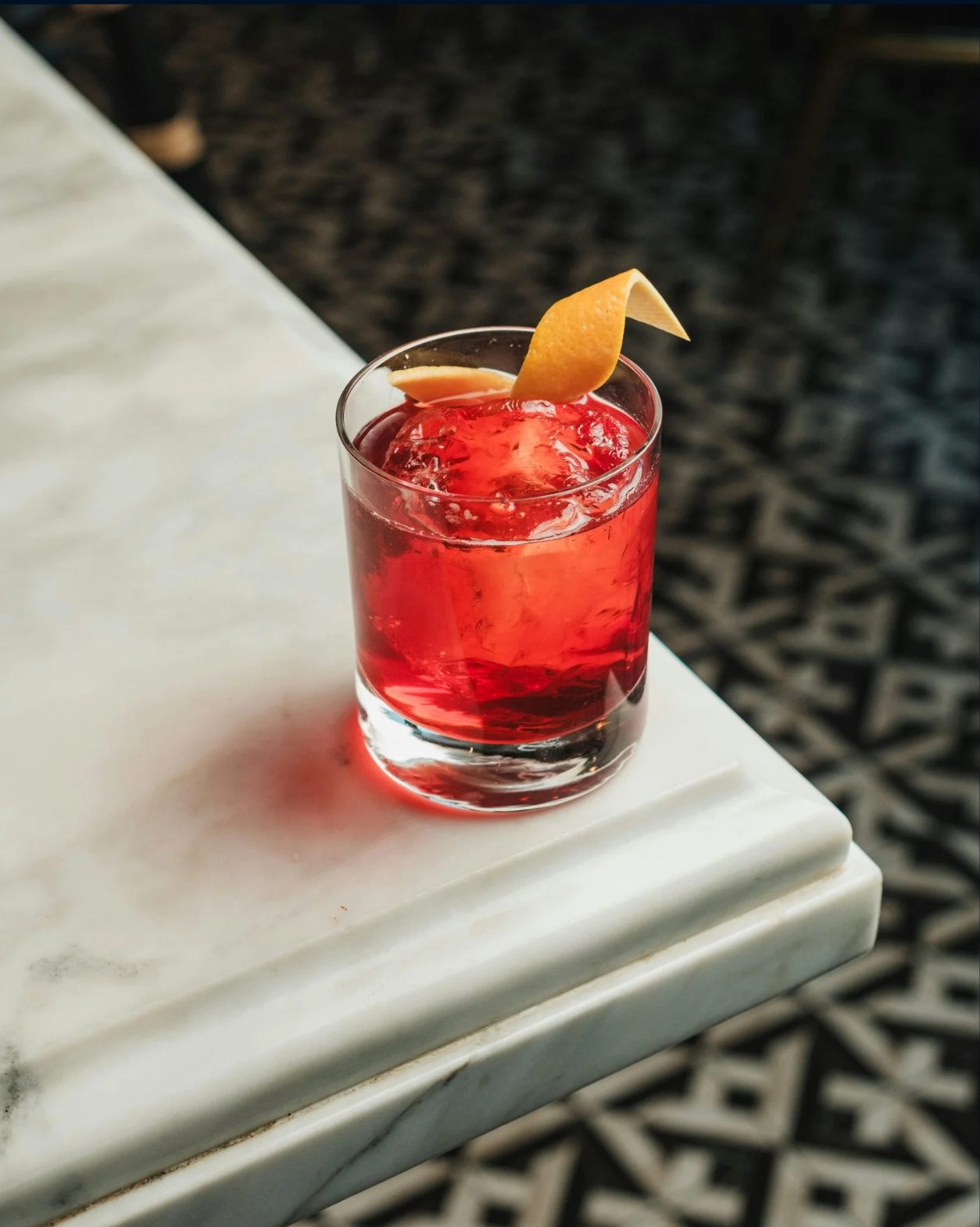 Red Opus Gin cocktail in a rocks glass with an orange peel garnish on a marble table